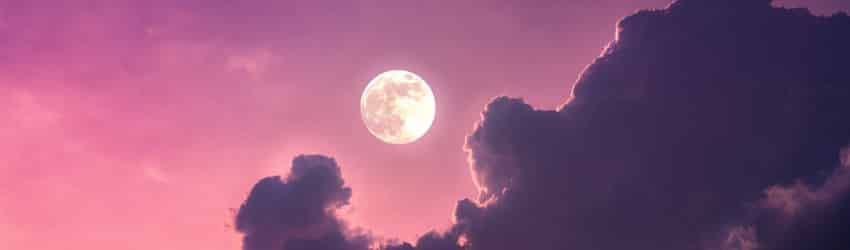 A Full Moon on a purple sky with dark purple clouds floating beneath the Moon.