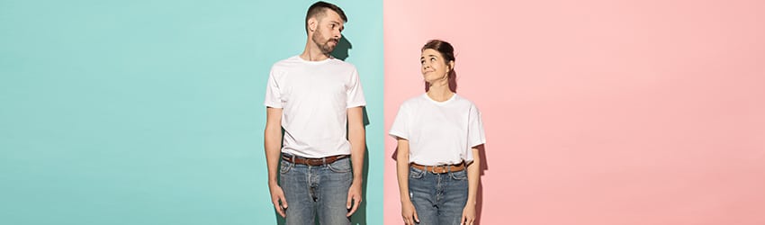 A man and a woman, both wearing white shirts, brown belts, and jeans, stand facing forward and look at each other sideways.