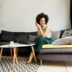 fashionable woman in a green skirt sitting on a modern grey couch smiling