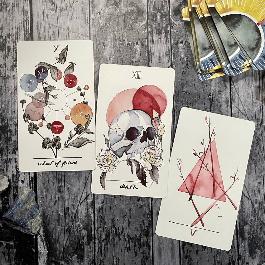 A sample Tarot spread on a wooden background featuring the Wheel of Fortune, Death, and 5 of Wands Tarot cards.