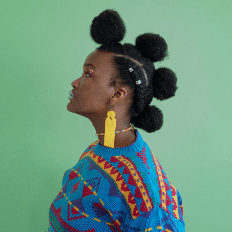 A black woman with a bright sweater stands with her side profile shown.