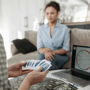 A person holding face-down Tarot cards sits in front of a computer with a birth chart.