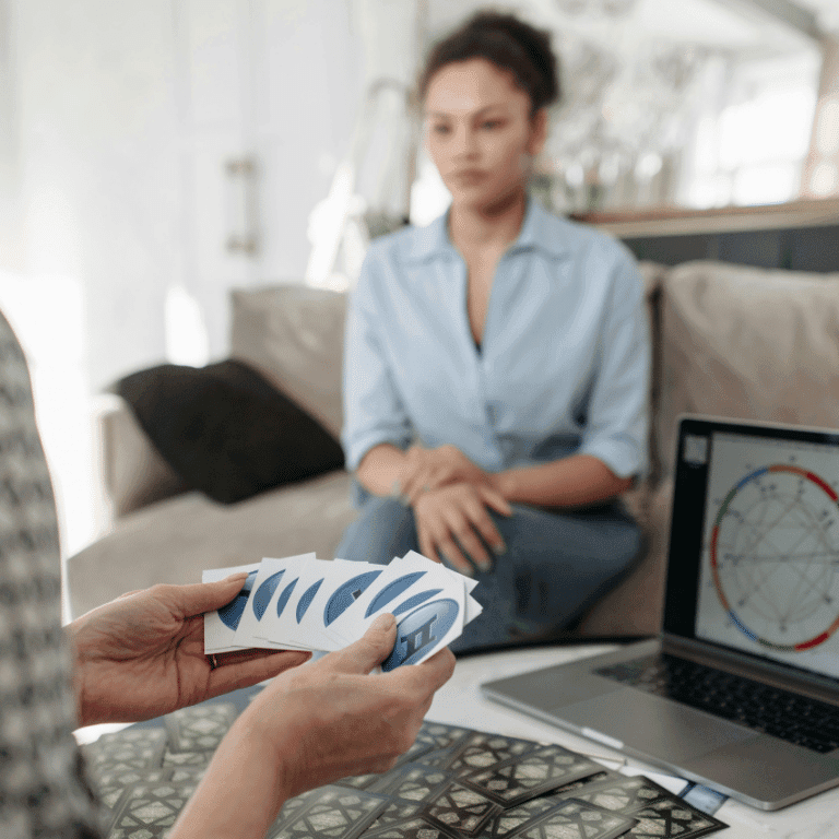 A person holding face-down Tarot cards sits in front of a computer with a birth chart.