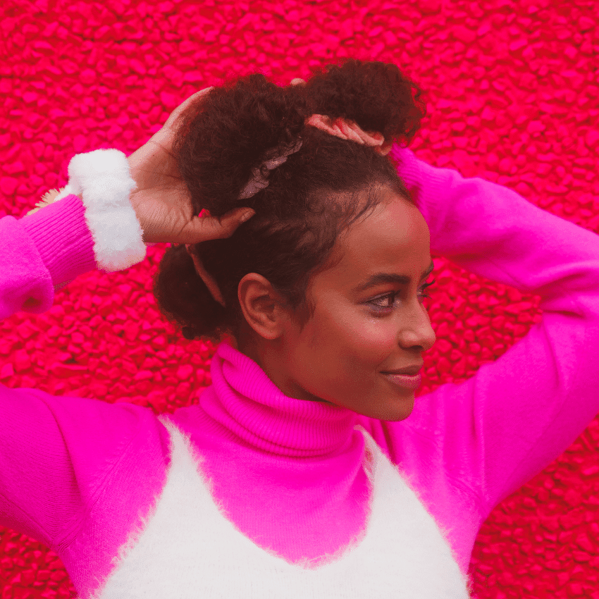 A black woman with two buns holds them and stares to her left.