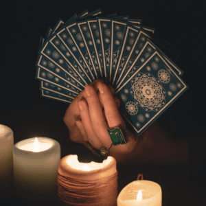 A hand holds a handful of Tarot cards, shown illuminated by candlelight.