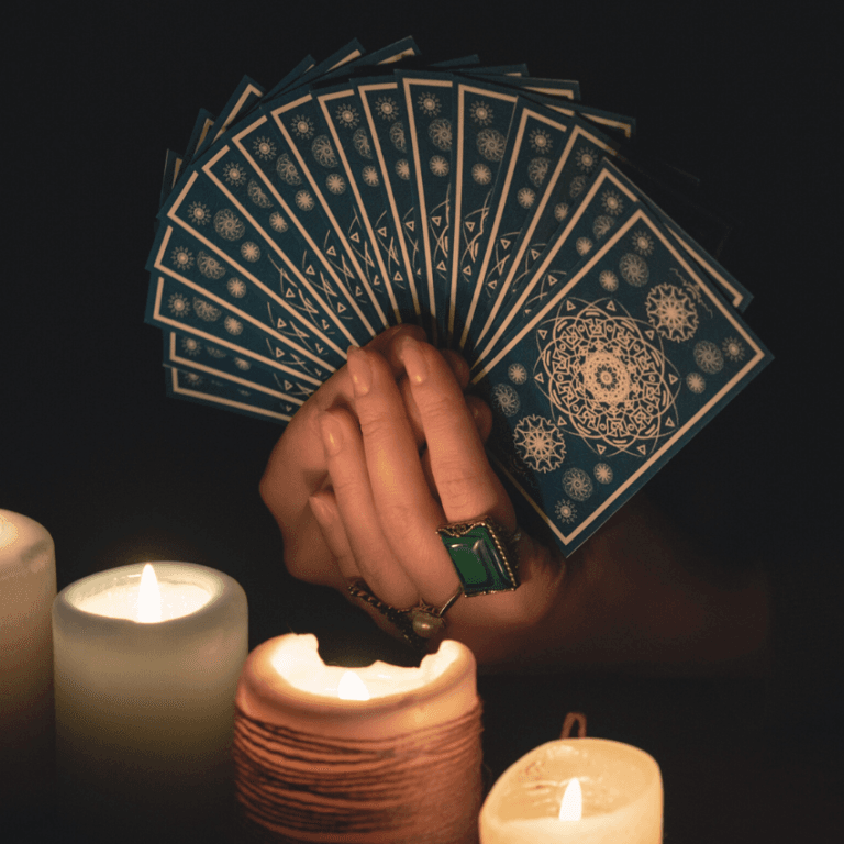 A hand holds a handful of Tarot cards, shown illuminated by candlelight.