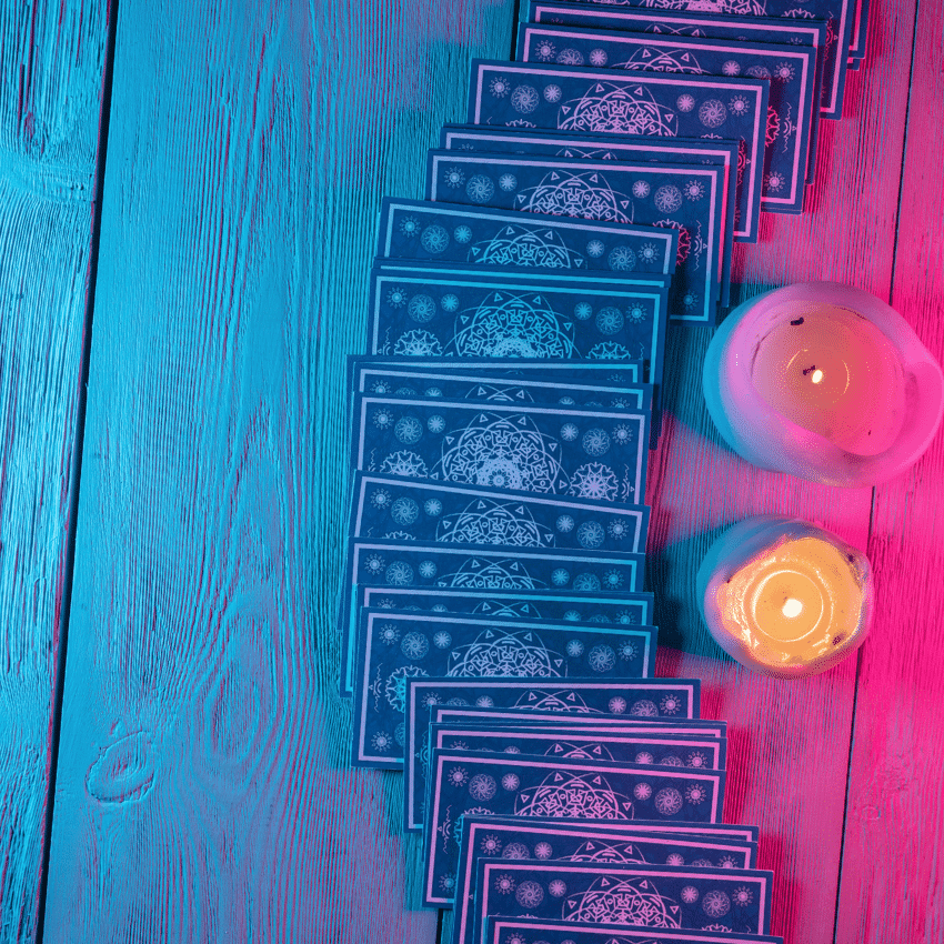 A line of Tarot cards face down next to 2 lit candles.